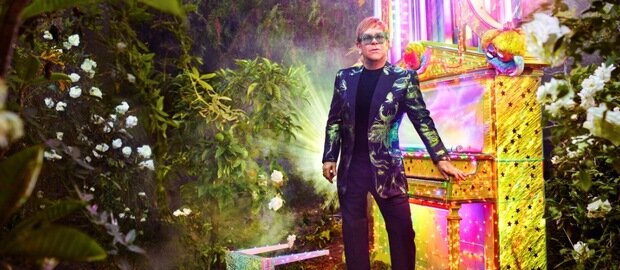 Sir Elton John steht in einem Garten vor einem Piano