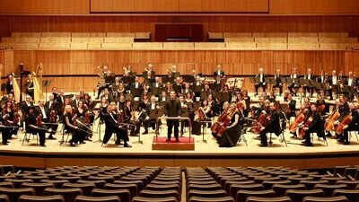 Die Musiker des London Philharmonic Orchestras und ihr Dirigent sitzen bzw. stehen mit ihren Instrumenten auf der Bühne