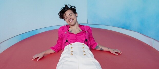 Harry Styles liegt auf einer rosa Scheibe und stützt sich auf seine Unterarme