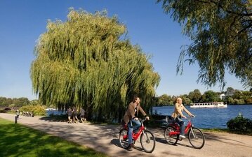 Ein Pärrchen genießt das traumhafte Wetter an der Alster und macht eine Tour mit dem Stadtrad.