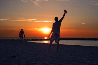 Zwei Jugendliche, die am Strand vor der Kulisse eines Sonnenuntergangs Frisbee spielen.