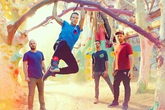 Ein Gruppenbild der Band Coldplay, bei dem Chris Martin lässig am Baum hängt.