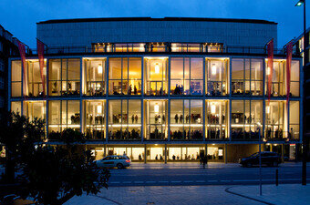 Das Gebäude der Hamburgischen Staatsoper in frontaler Ansicht und bei nächtlicher Beleuchtung