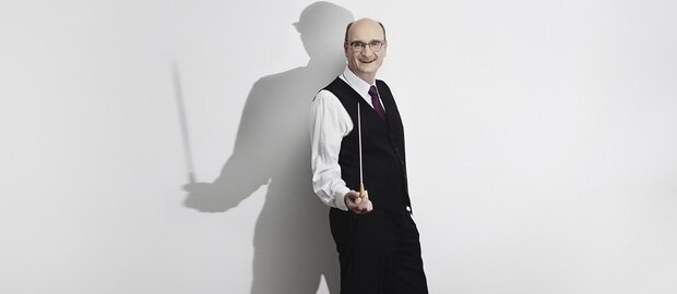 Andrew Manze vor einer weißen Wand mit einem Taktstock in der Hand