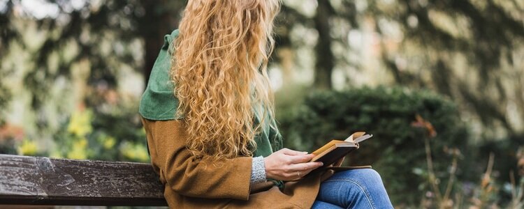 Eine junge Frau sitzt auf einer Bank im Wald und liest ein Buch