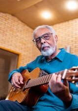 Gilberto Gil spielt eine Akustik Gitarre und sieht in die Kamera