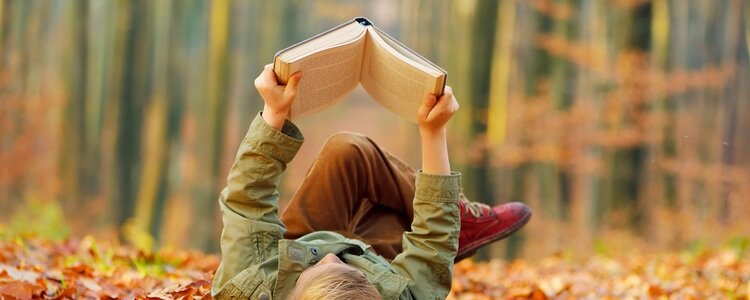 Kleiner Junge liegt im Laub und liest ein Buch