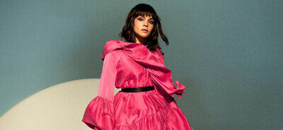 Norah Jones in einem roten Kleid vor blau grauer Wand.